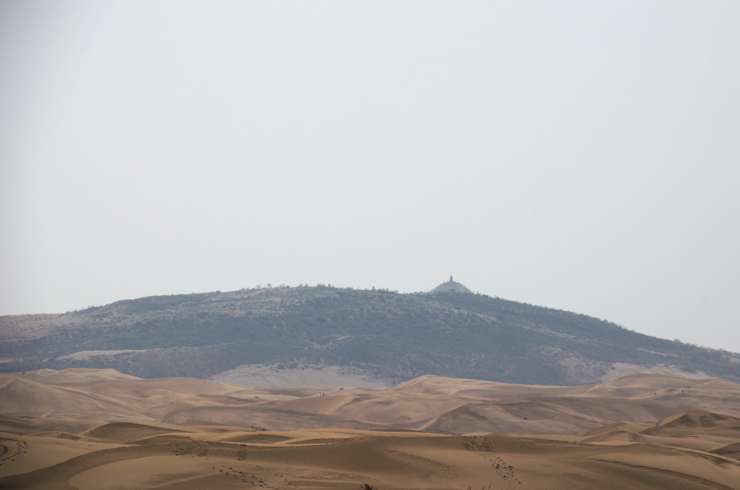 Sand dunes of the Kubuqi Desert with a distant stupa on a low ridge