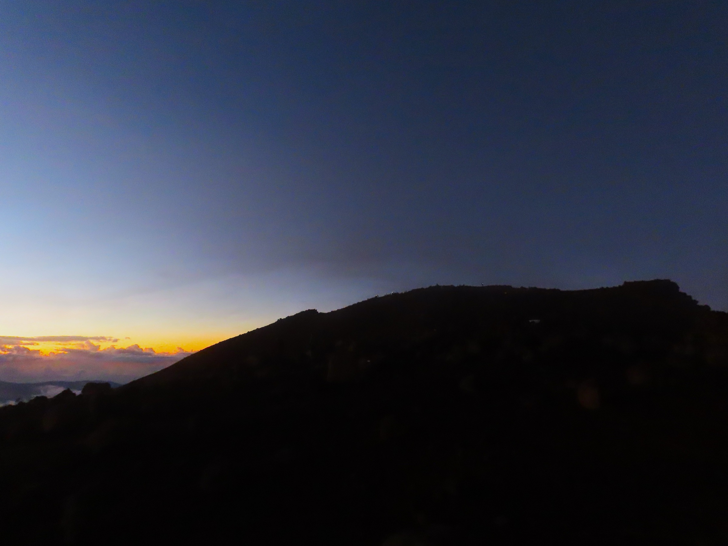 Lever du soleil depuis le sommet du Piton des Neiges, avec des bombes volcaniques au premier plan et des nuages remplissant les cirques en contrebas