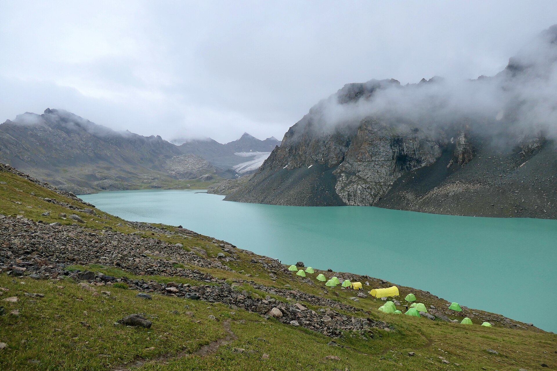 Small trekking tents beside Ala-Kul beneath cloud-wrapped peaks