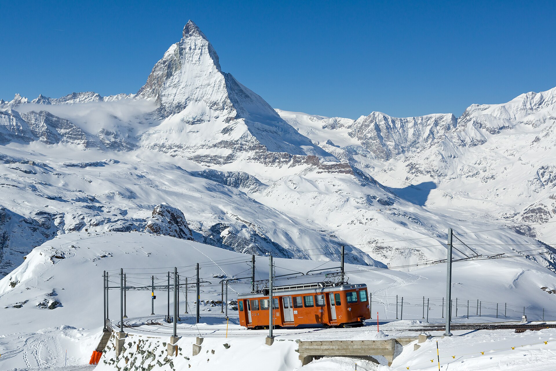 A red Gornergrat railway car crossing snowy slopes beneath the Matterhorn