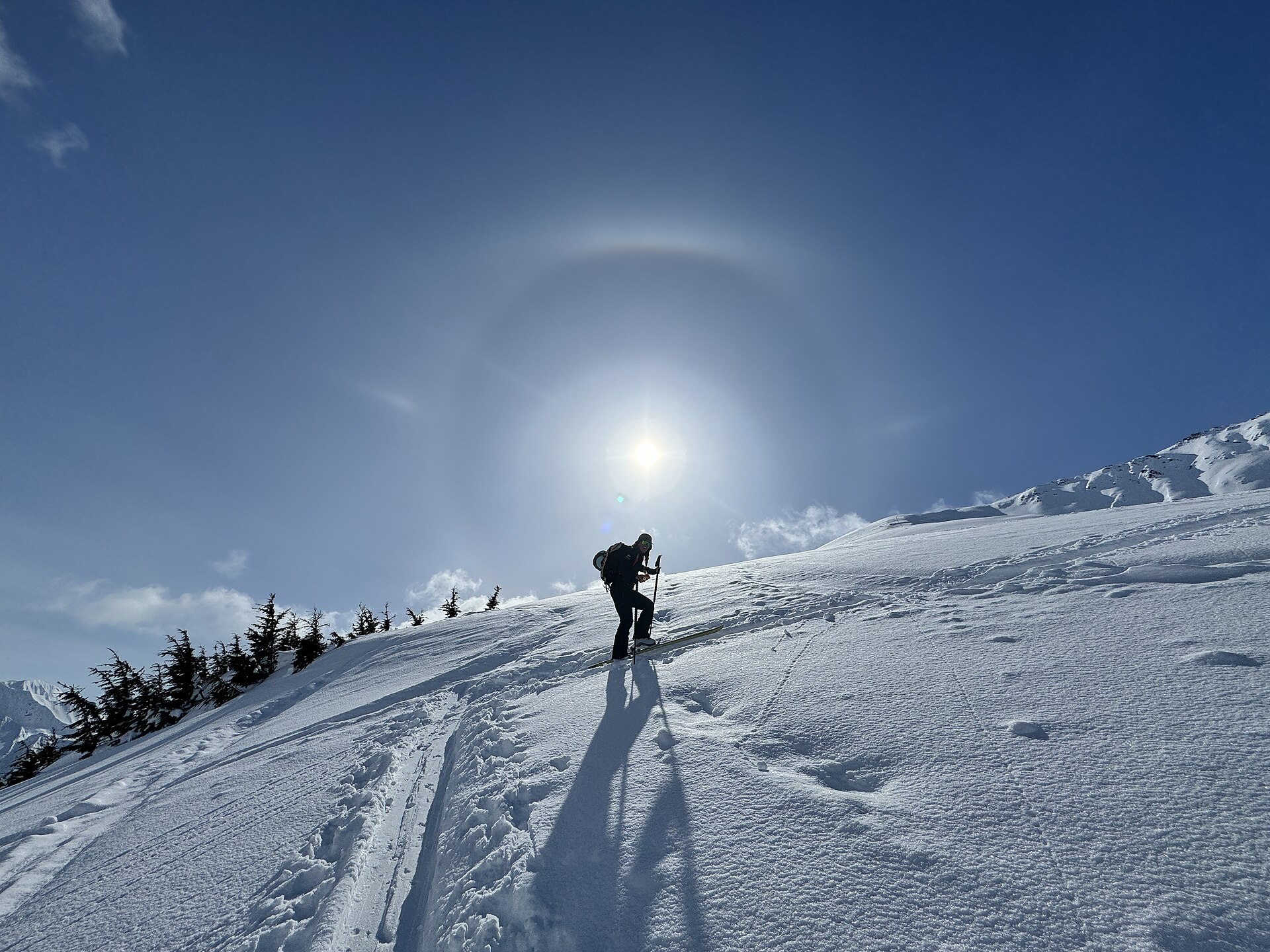 A lone ski tourer climbing beneath a sun halo in the Chugach Mountains