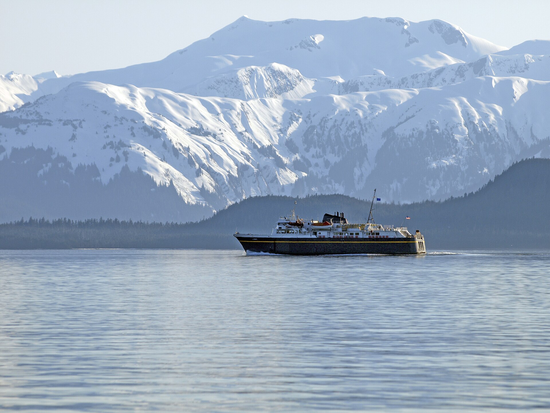A small ship crossing calm water beneath the snow-covered Chilkat Range
