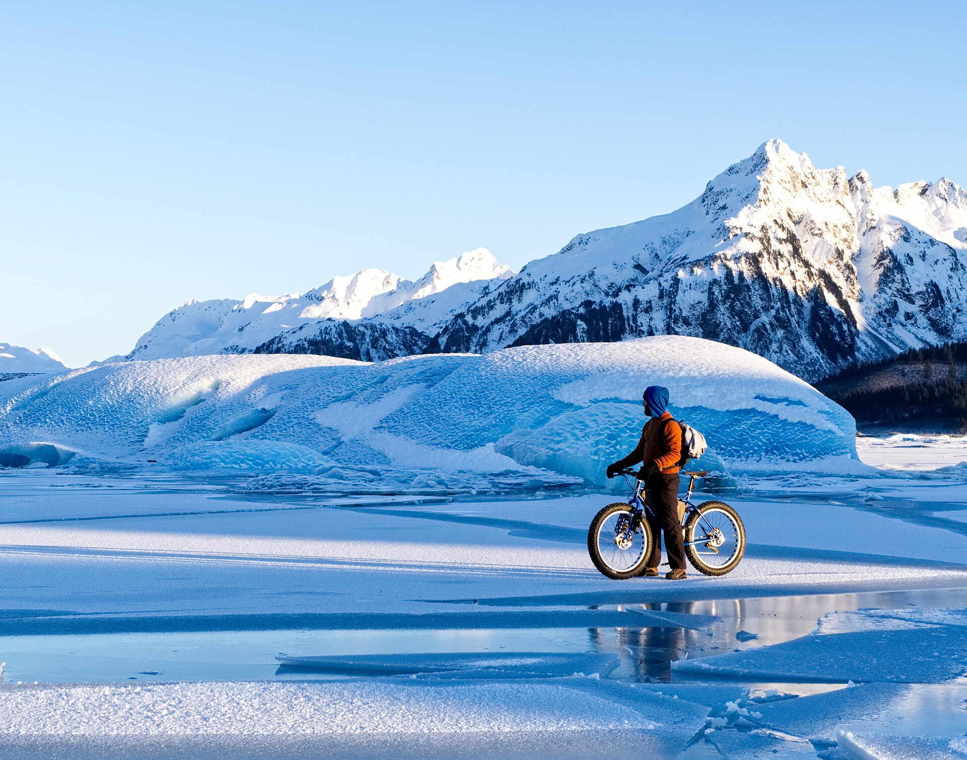 A fat-tire cyclist riding across a frozen lake below Sheridan Glacier near Cordova