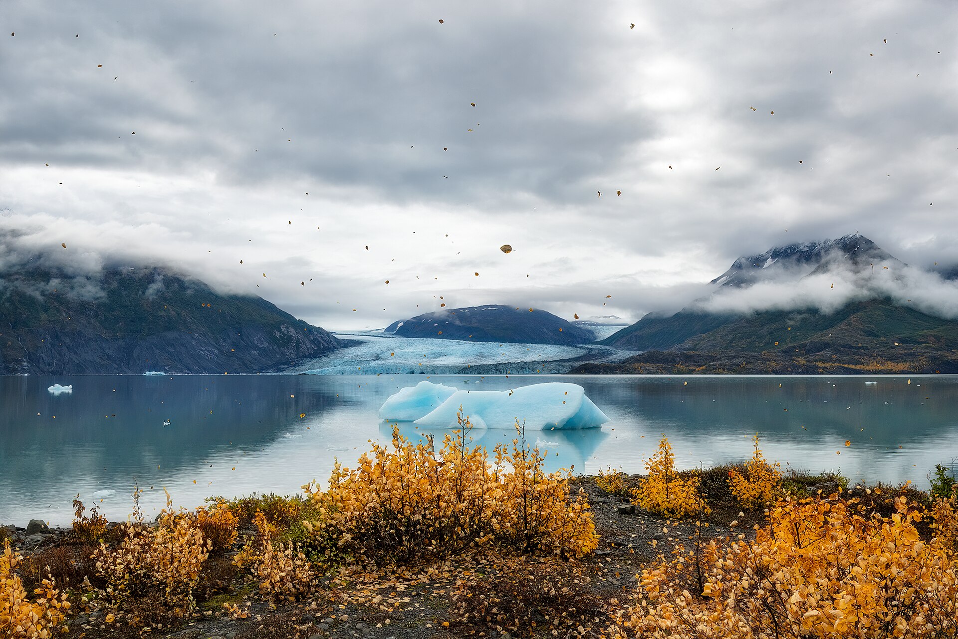 Blue glacial ice floating in Inner Lake George beneath cloud-covered Alaska mountains