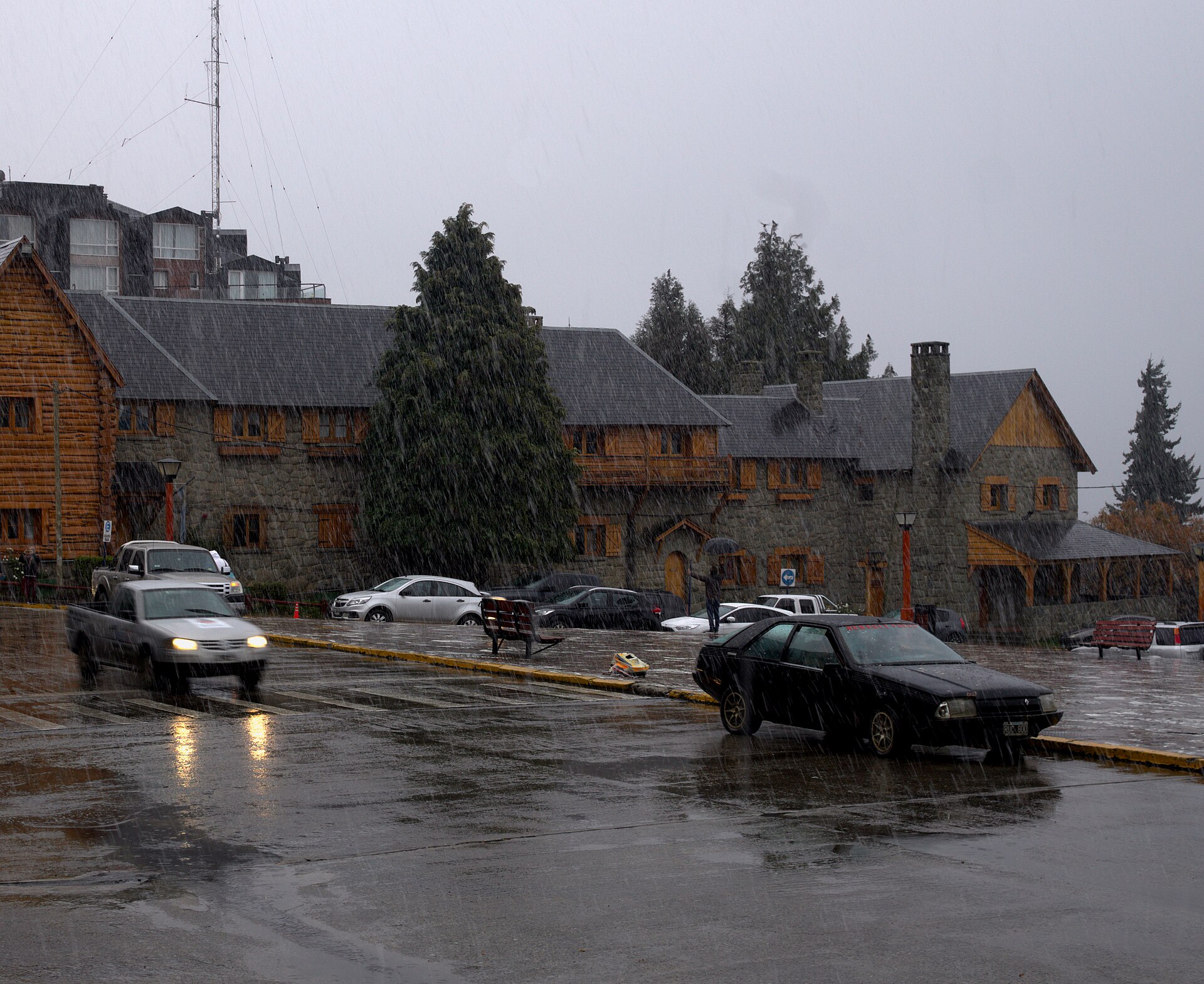 Des voitures passant devant les bâtiments de pierre et de bois du Centre civique de Bariloche sous de fortes précipitations