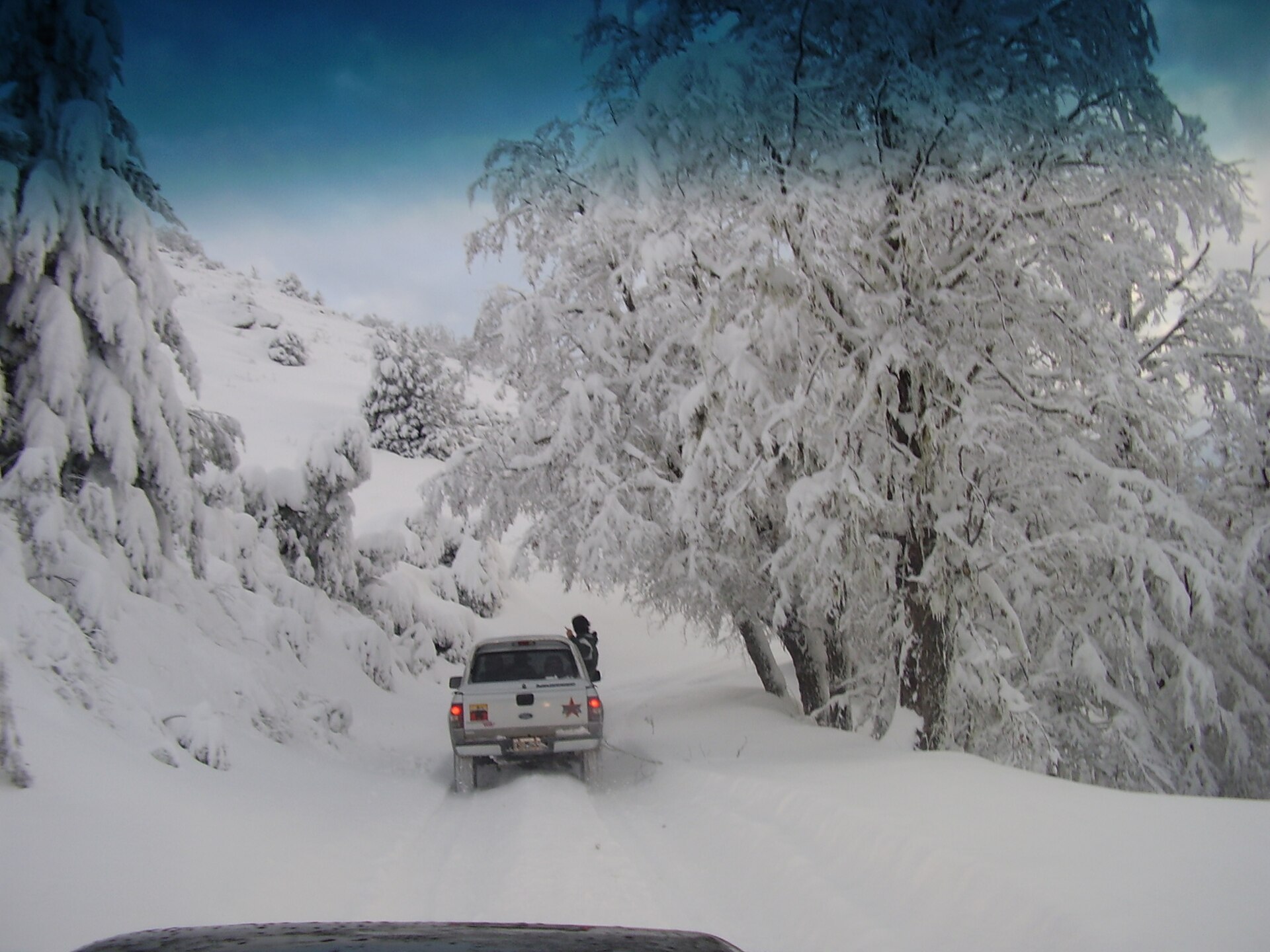 Un véhicule suivant une route étroite à travers la neige profonde et la forêt blanche près de Bariloche