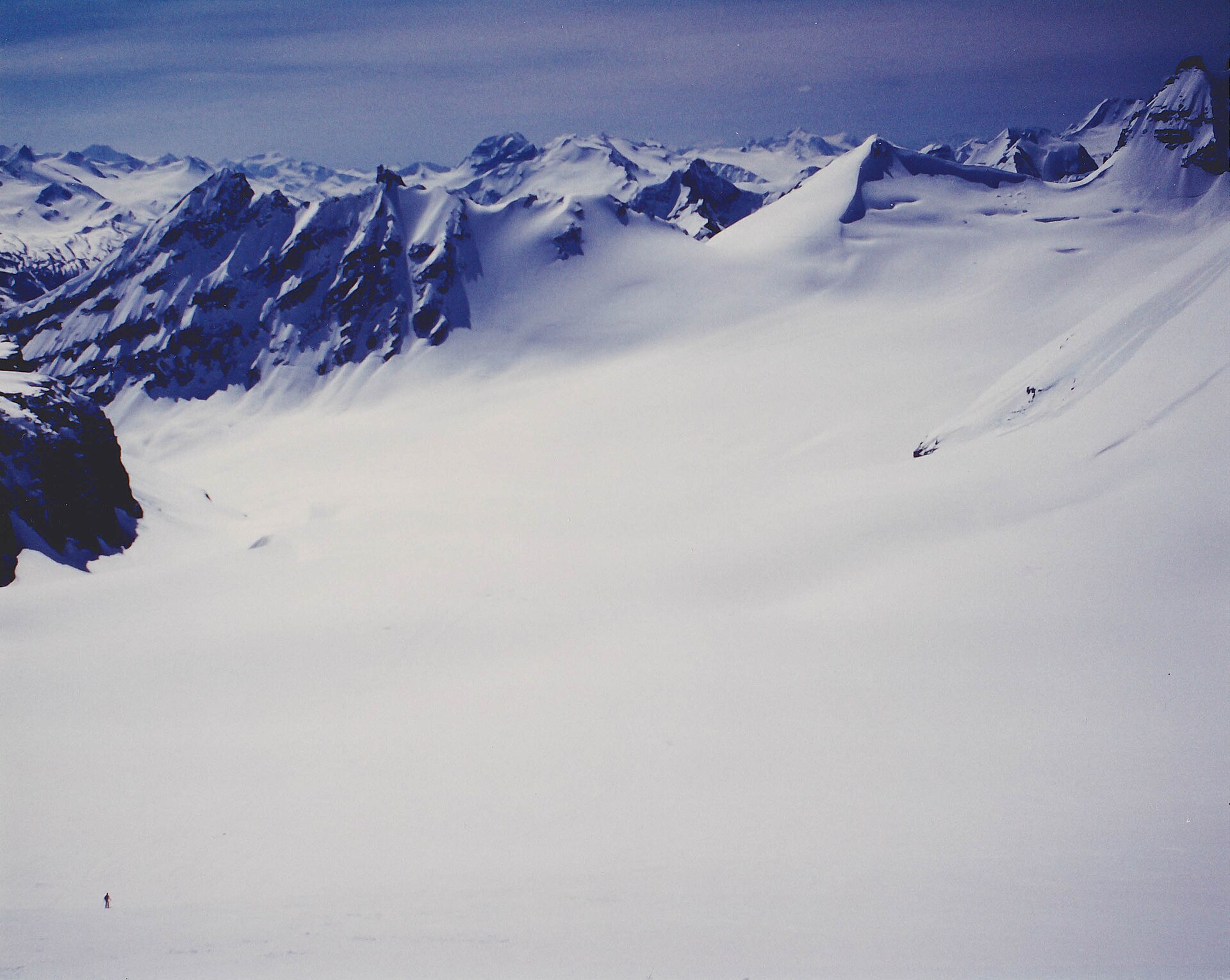 Un skieur solitaire traversant un vaste cirque glaciaire sous des sommets déchiquetés, dans les Selkirk