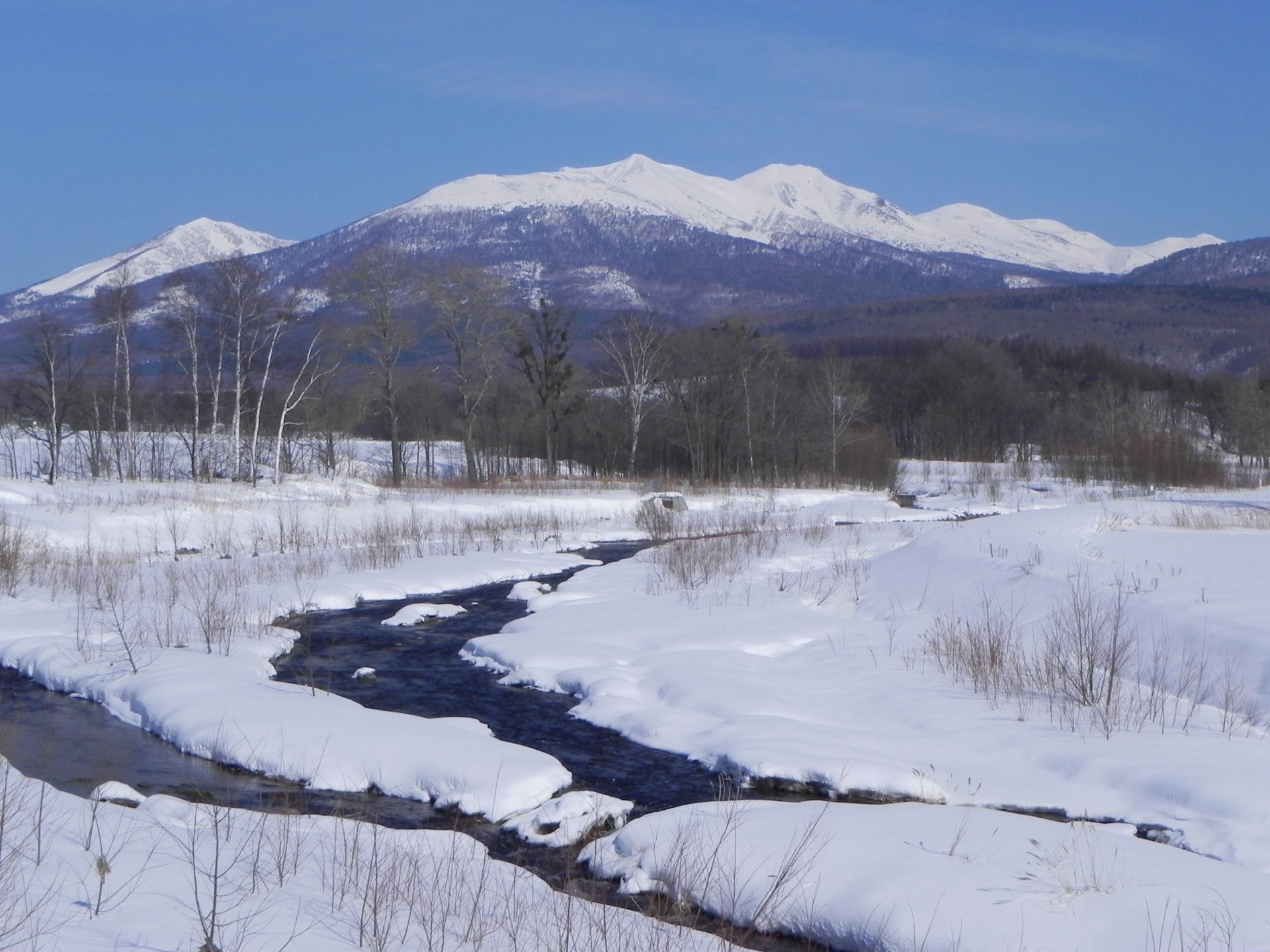 A dark river winding through snowfields below the central Hokkaido mountains