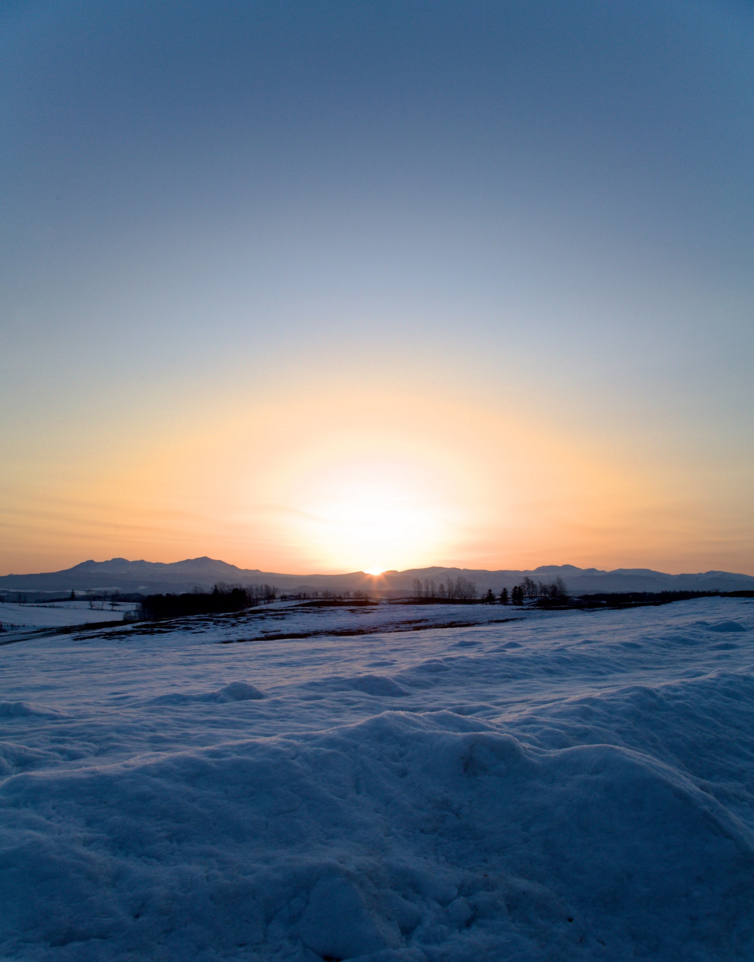 Dawn breaking over the snow-covered fields of Biei, with a low mountain skyline on the horizon