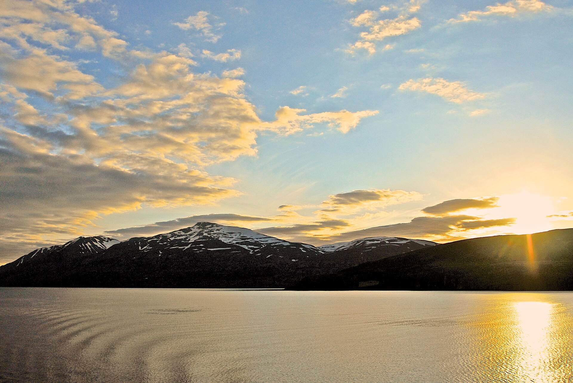 Low golden light behind a snow-streaked mountain in East Iceland