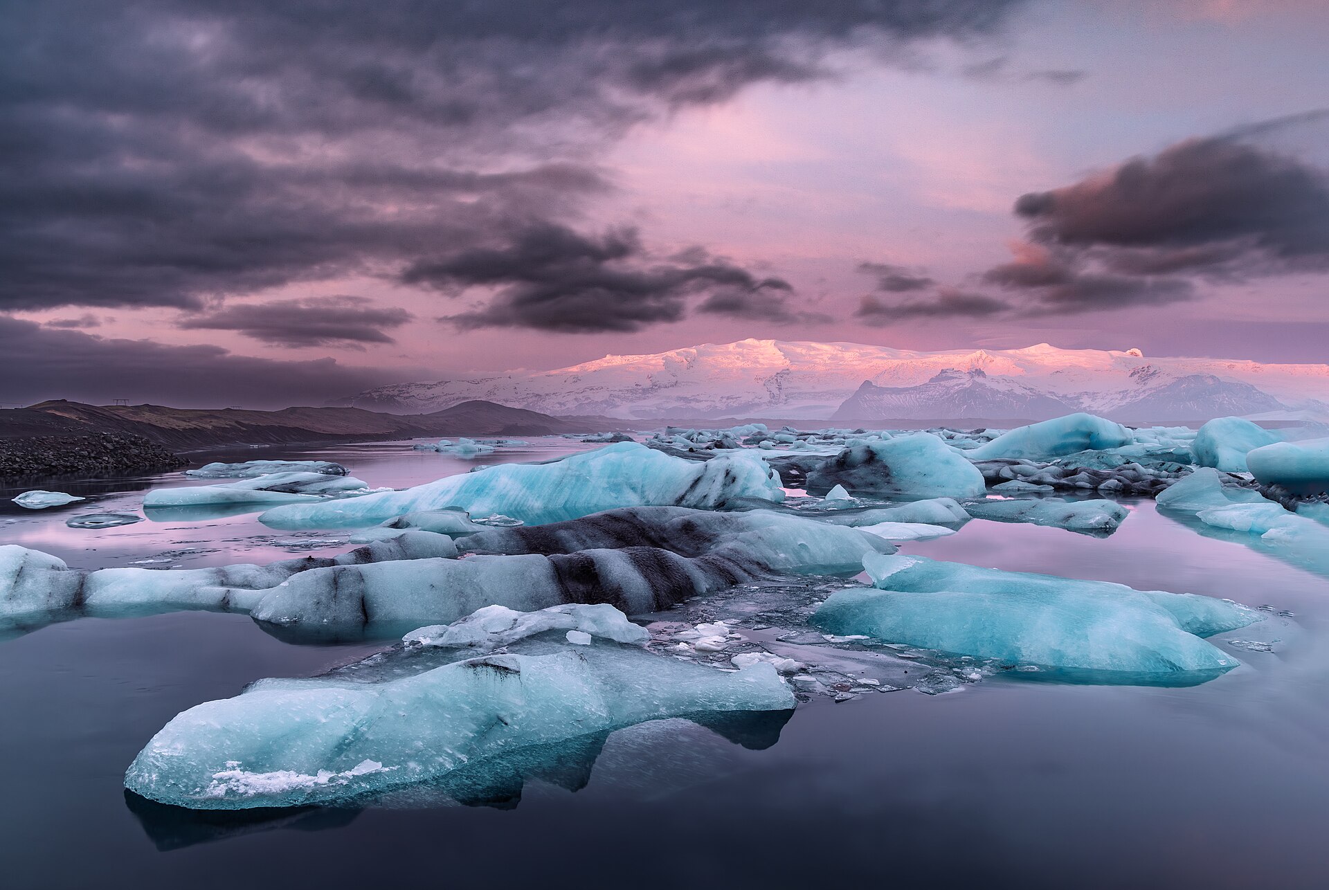 Blue icebergs floating in Jökulsárlón beneath a pink dawn sky