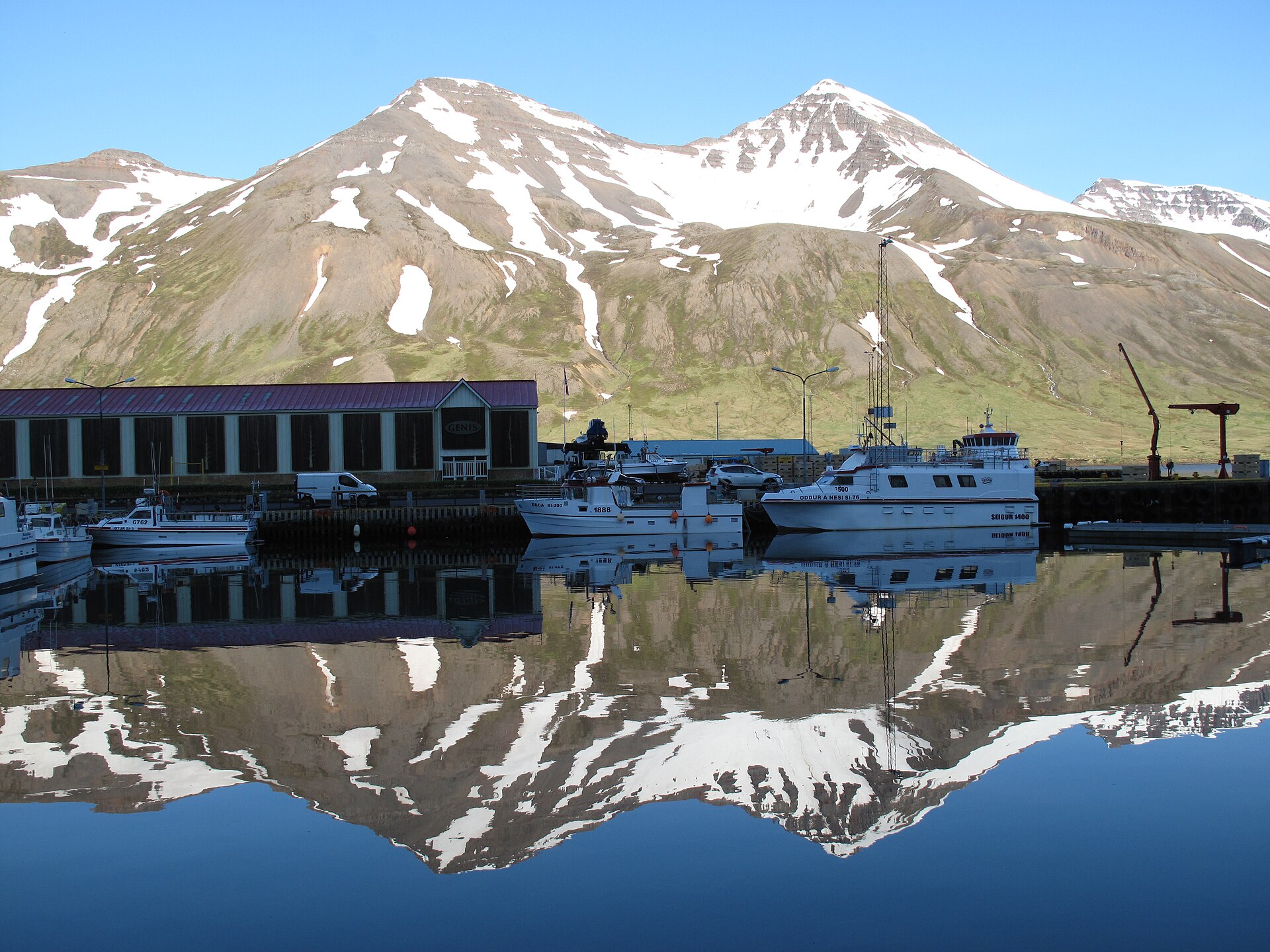 Snow-streaked mountains reflected in calm water at Siglufjörður