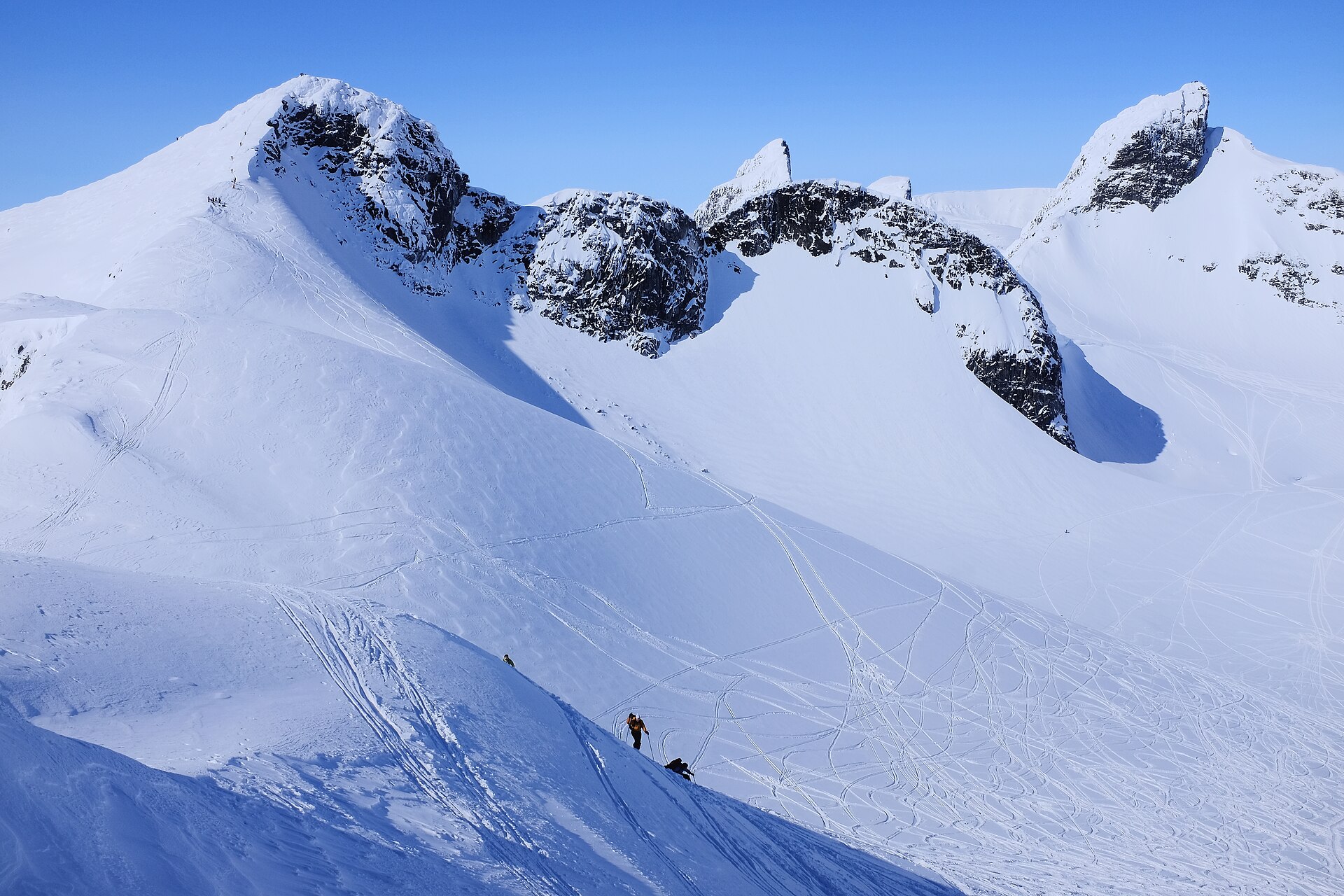 Ski tourers climbing a snowy ridge above Bjørnbrean in Jotunheimen