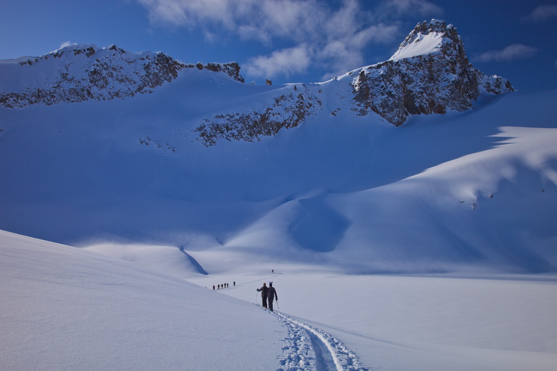 Des randonneurs à ski suivant une trace de montée sous les sommets enneigés des Selkirk