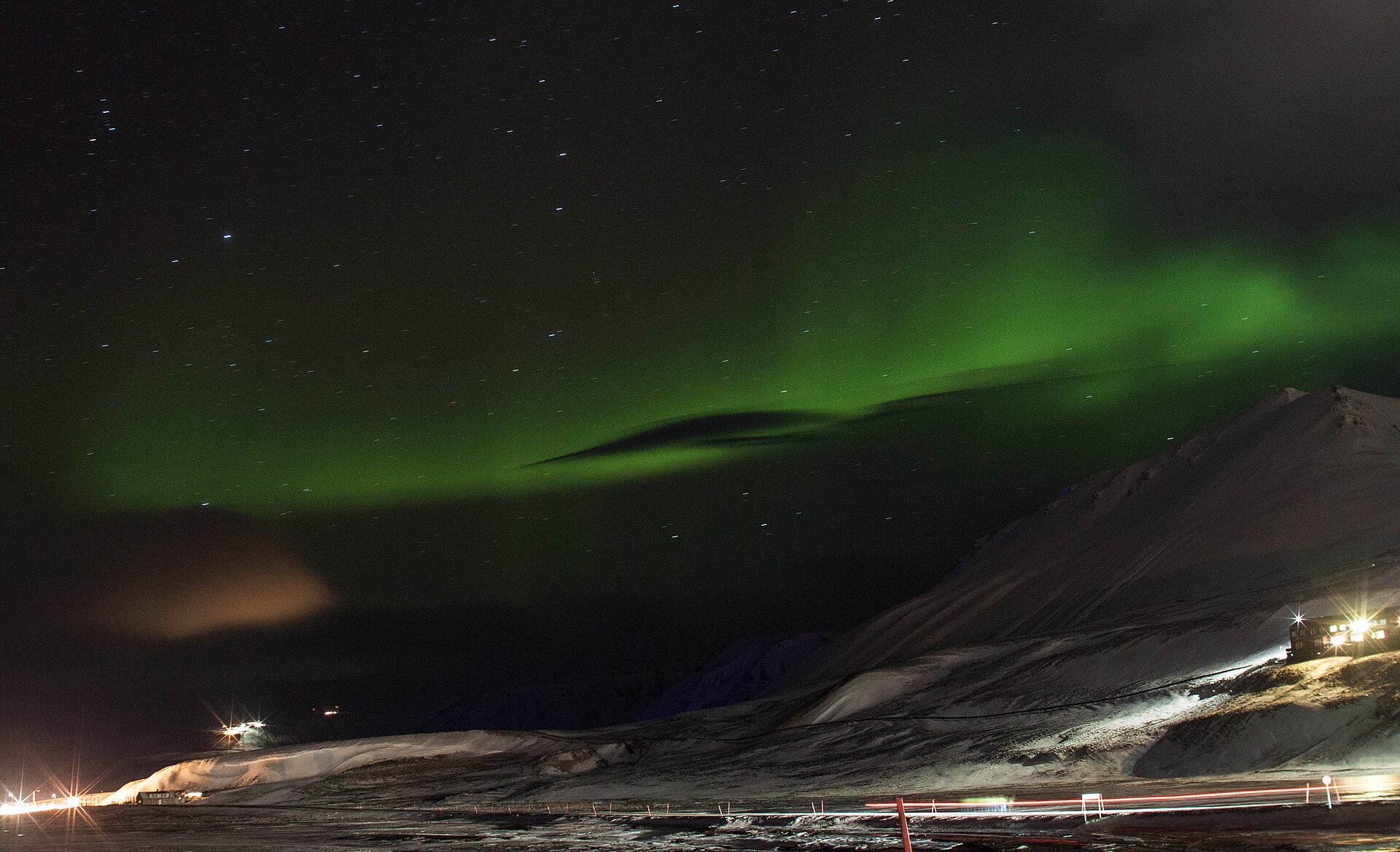 Green aurora above snowy mountains and lights in Svalbard