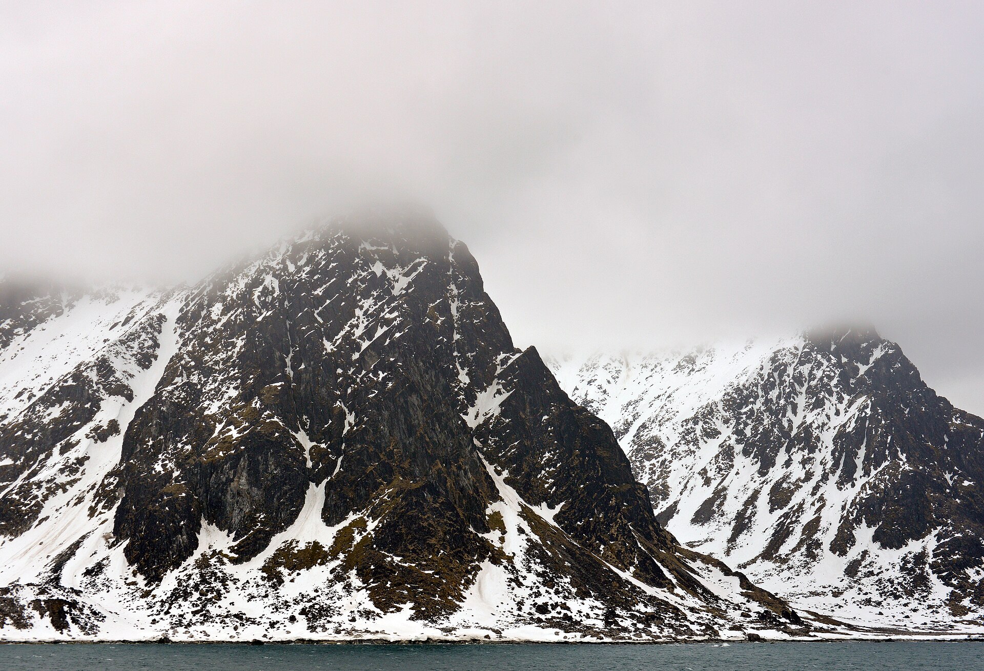 Snow-covered mountains rising sharply from Magdalenefjorden in early June