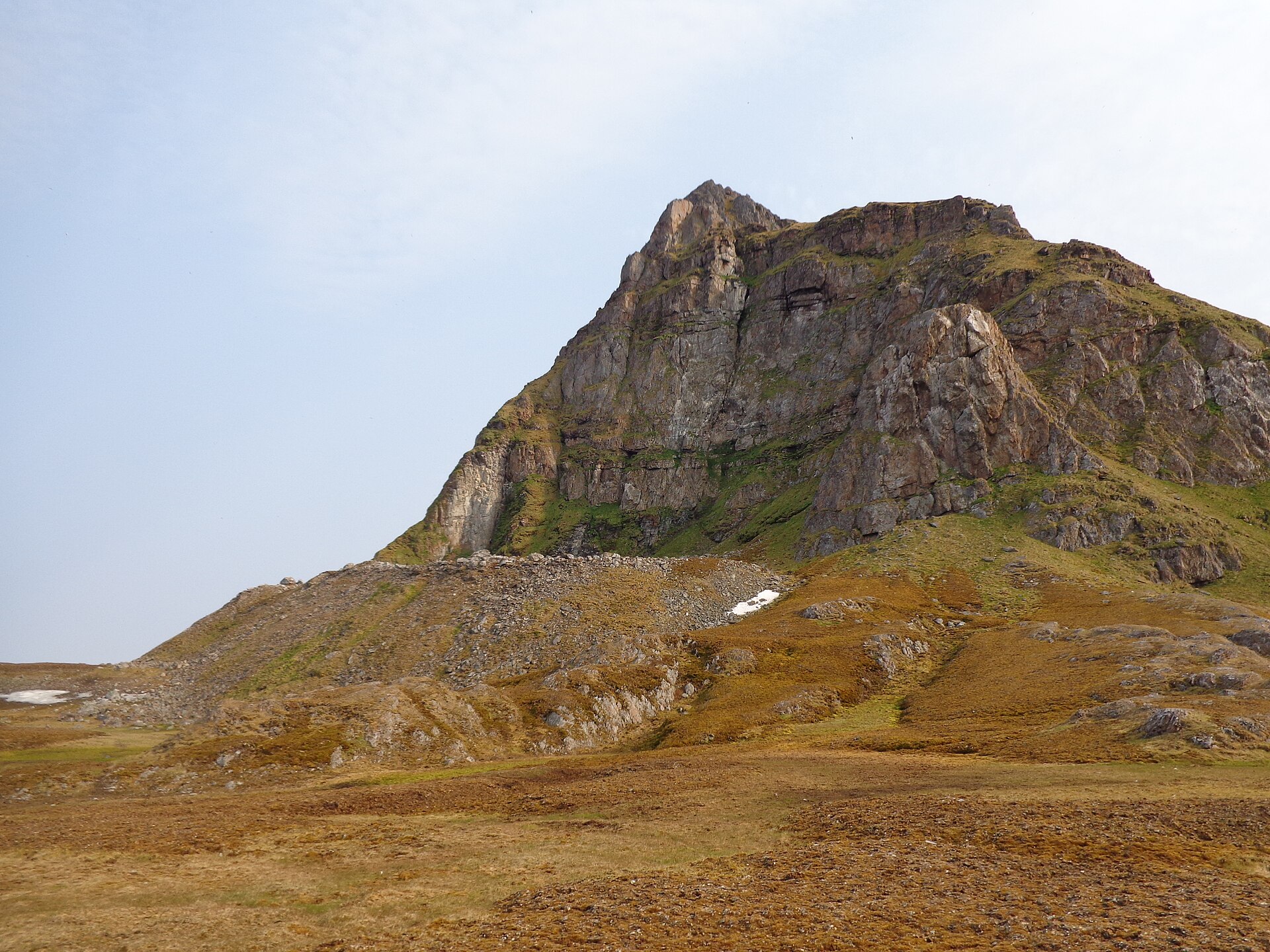 A steep, isolated mountain on Prins Karls Forland beneath a pale Arctic sky
