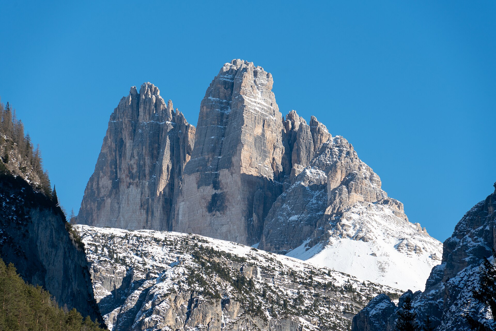 Les Tre Cime di Lavaredo dressées au-dessus de pentes enneigées, sous un ciel d'hiver bleu