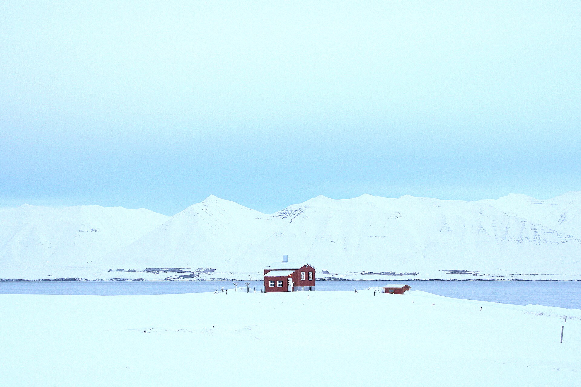 A small red cabin isolated in snow beside the water at Framnes near Dalvík