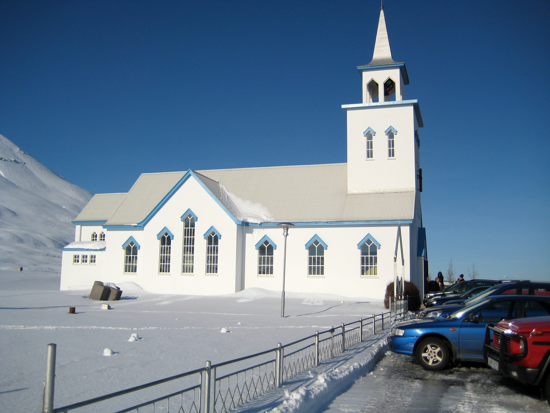 White Dalvík church surrounded by deep snow beneath blue sky
