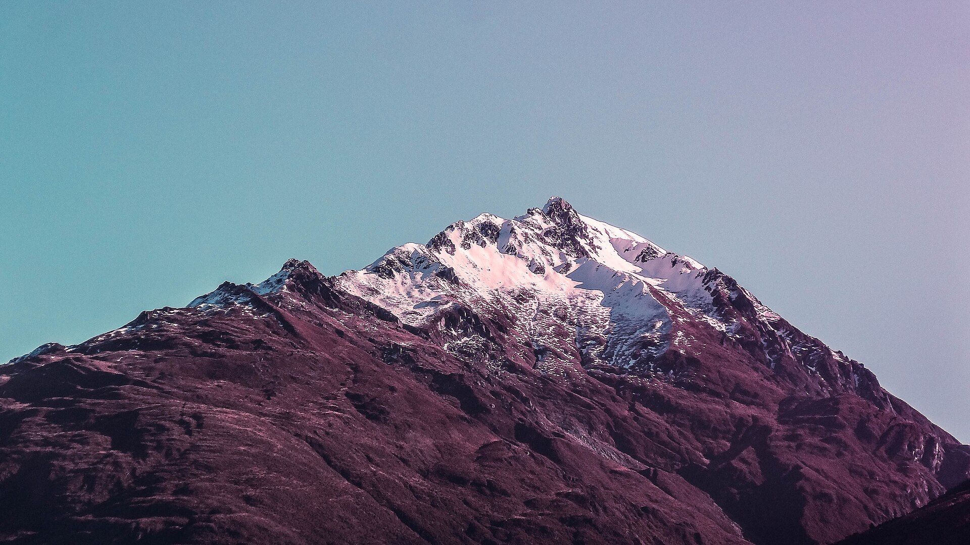 A snow-streaked peak near Wānaka glowing purple in evening light
