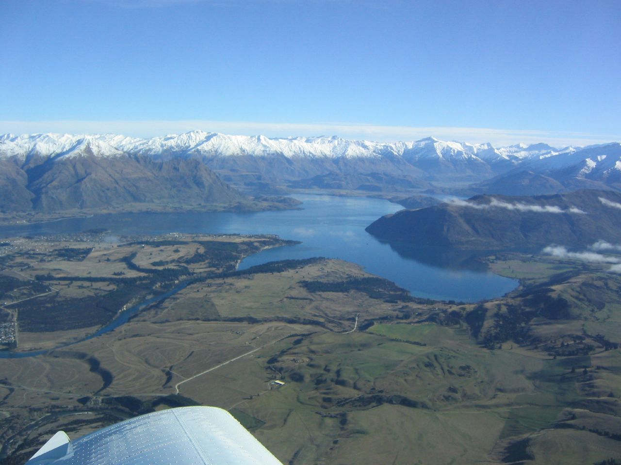 Aerial view across the Wānaka basin toward lakes and snow-covered mountains