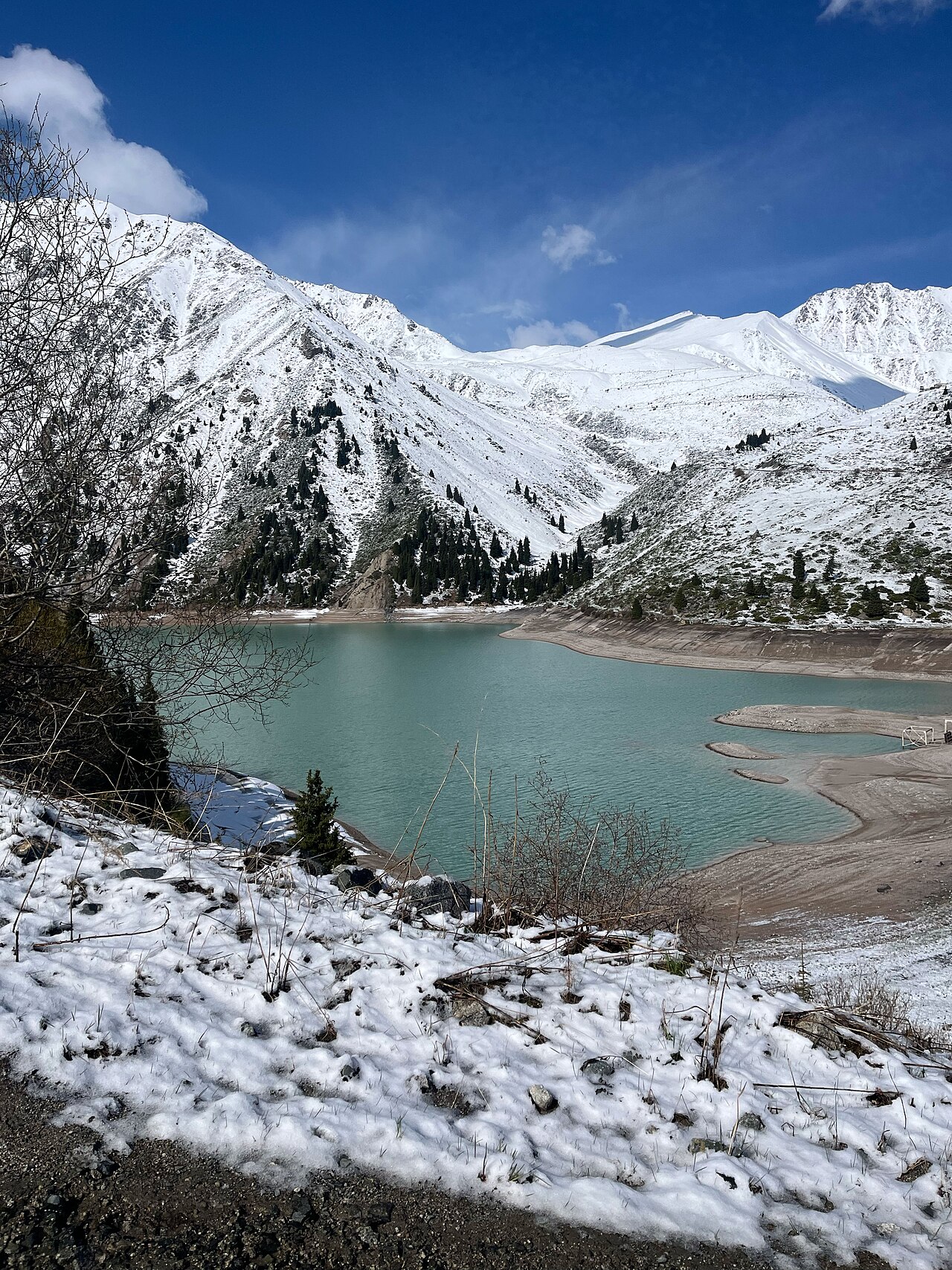 Turquoise Big Almaty Lake enclosed by snowy winter slopes