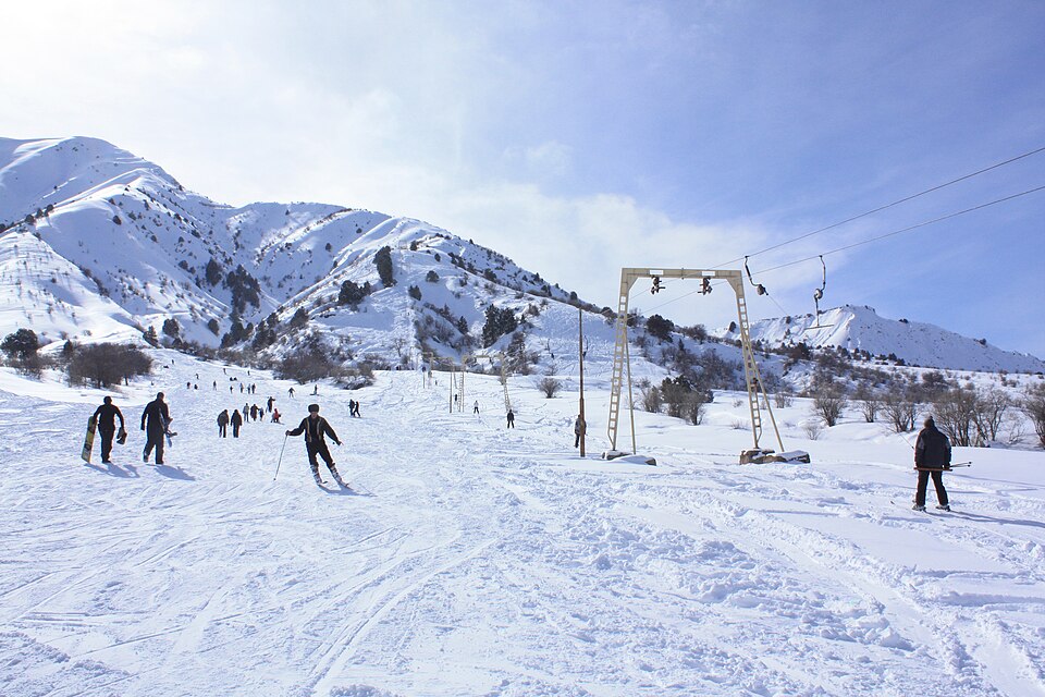 Skiers and a surface lift beneath snowy Chimgan slopes
