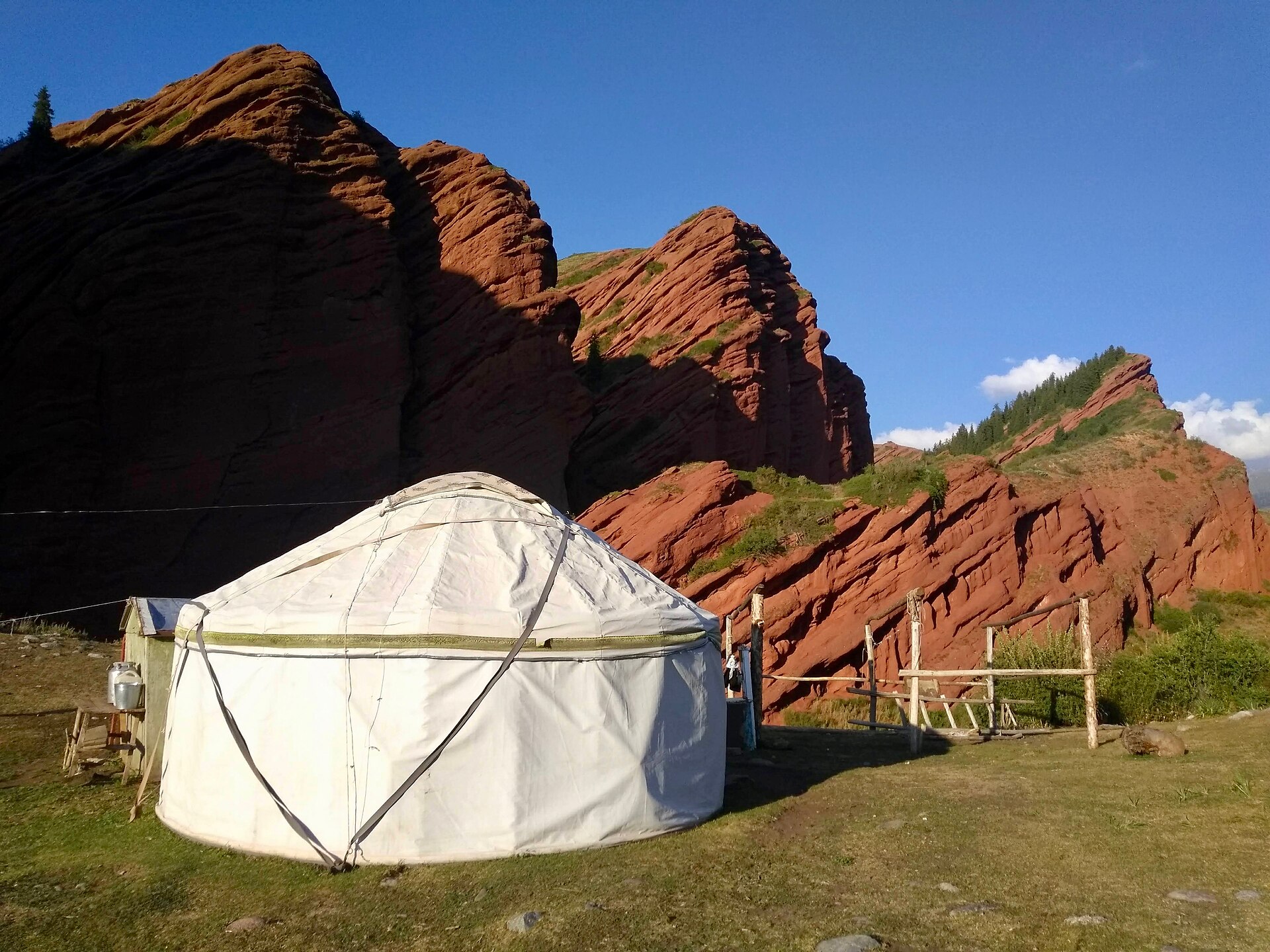 A white Kyrgyz yurt beneath red mountain cliffs in the wider Karakol region