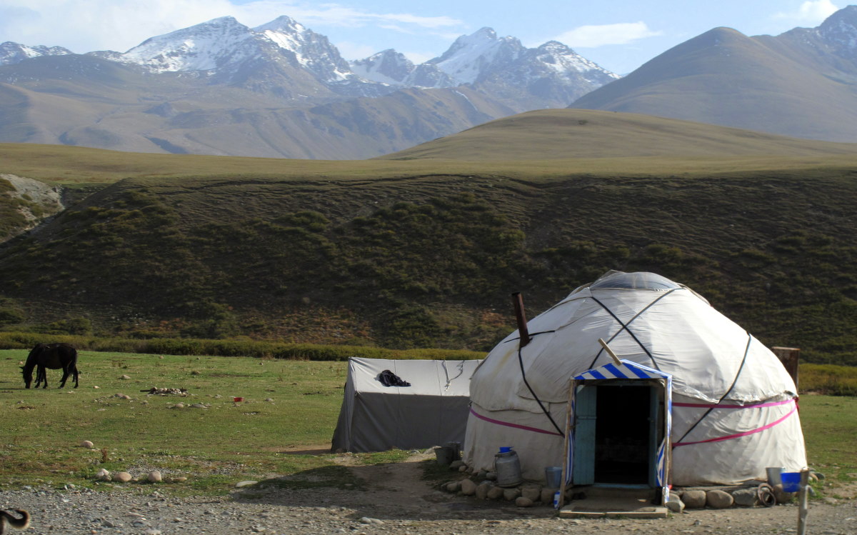 A white yurt on open pasture beneath the Suusamyr mountains