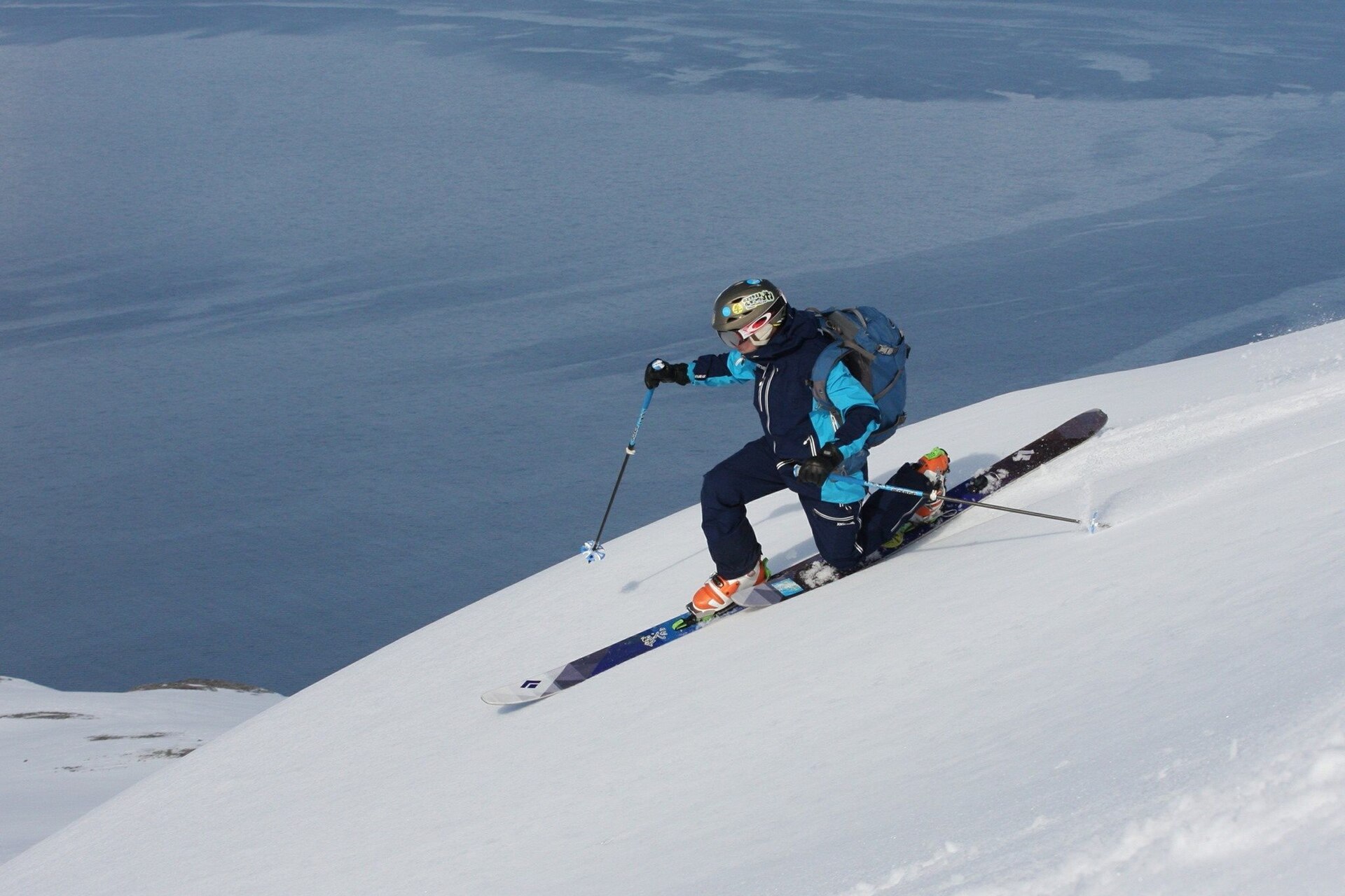 A skier making a telemark turn on a steep snow slope above the sea near Lyngen