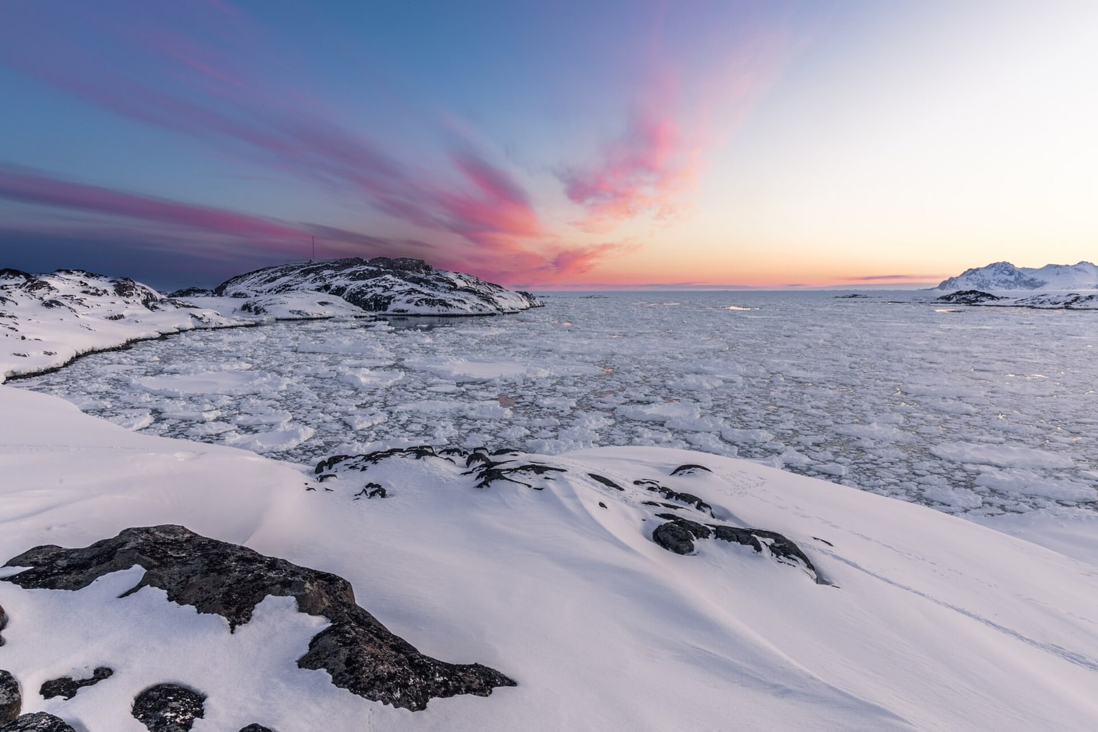 Blue pack ice and snowy mountains after sunset in East Greenland