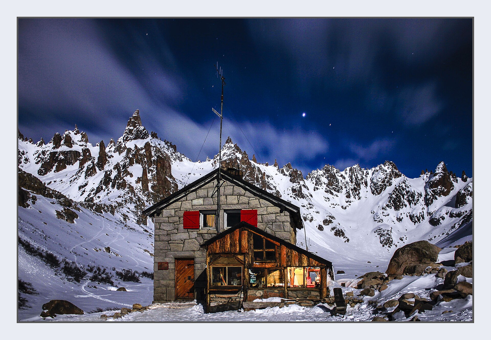 Refugio Frey glowing at night beneath snow-covered granite spires