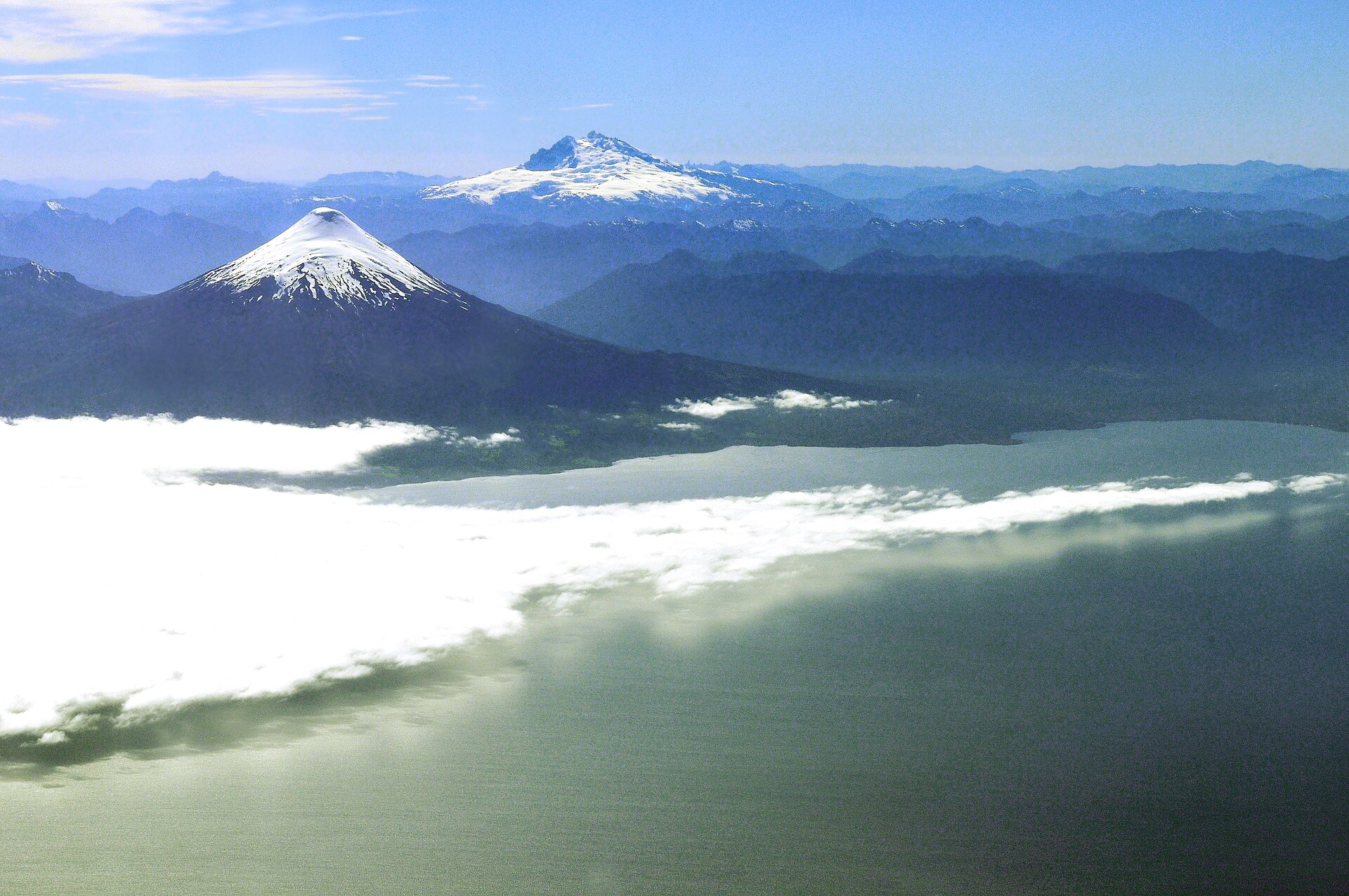 Aerial view of the Chilean Lake District with snow-covered volcanoes above cloud