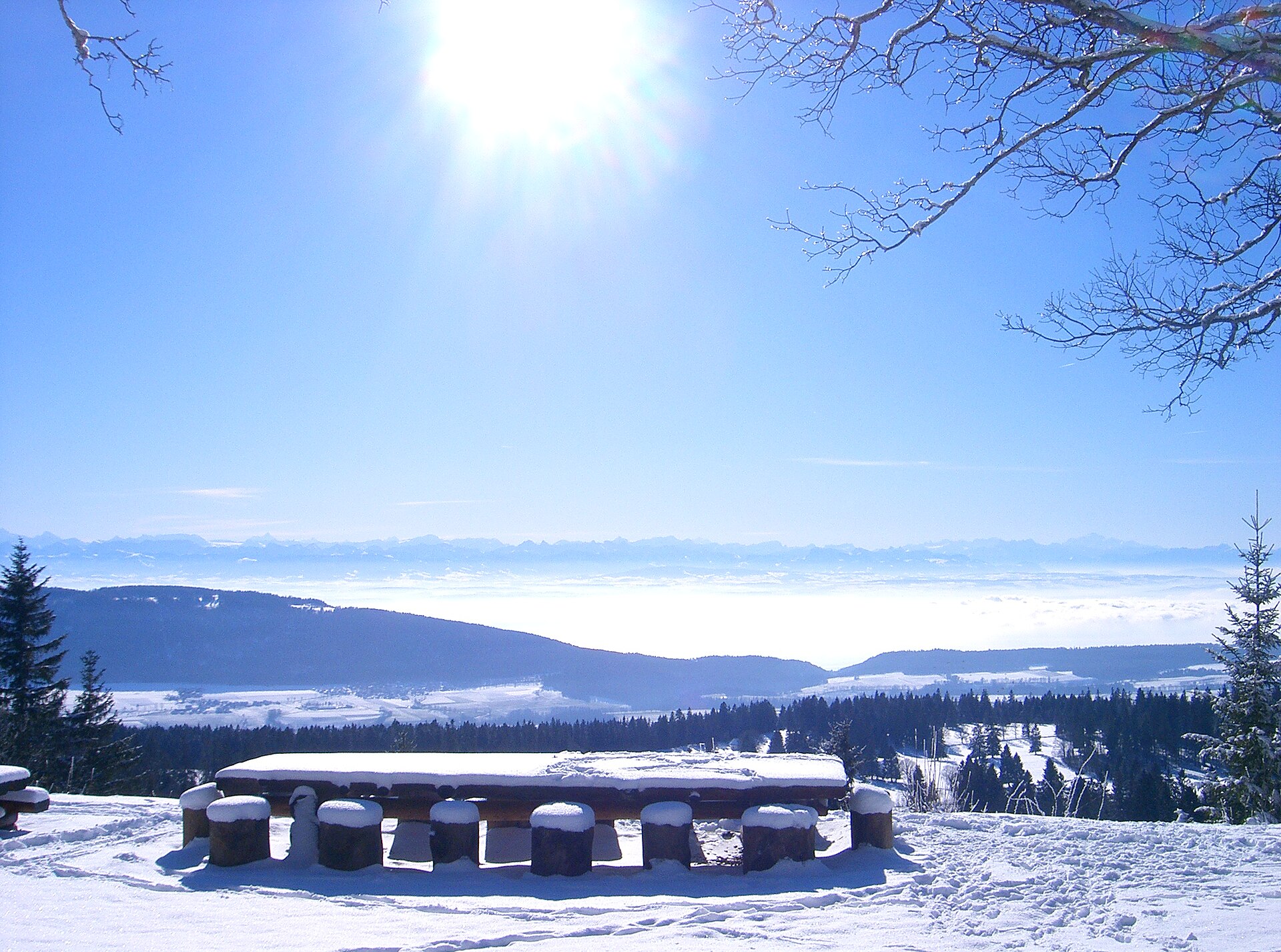 Snow-covered fields and buildings in the Swiss Jura with the Alps on the horizon